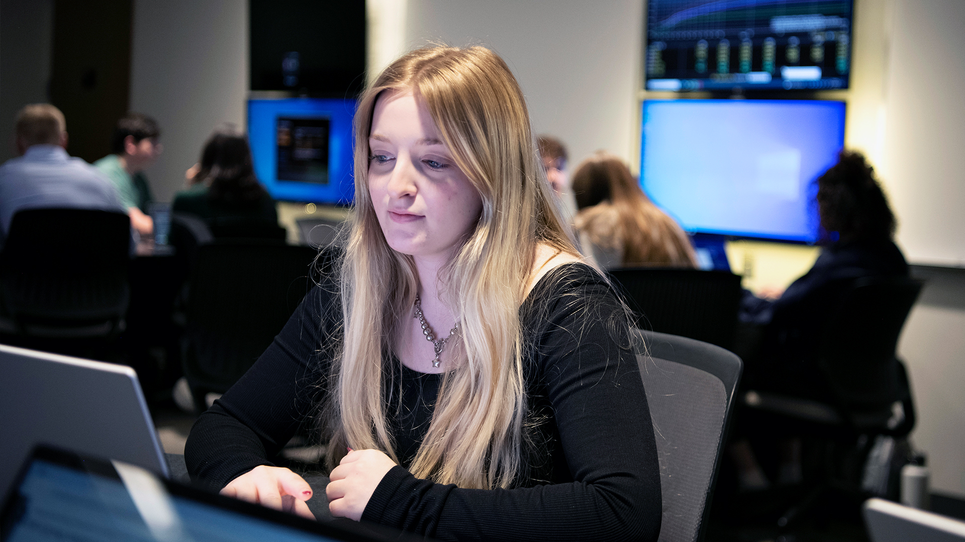 A Drake Artificial Intelligence Major studies a laptop in a campus computer lab, face illuminated by the glow