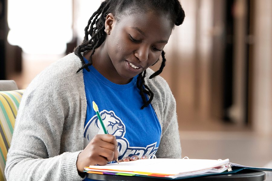 A Drake Artificial Intelligence student sits at a desk while taking notes with a pencil and binder