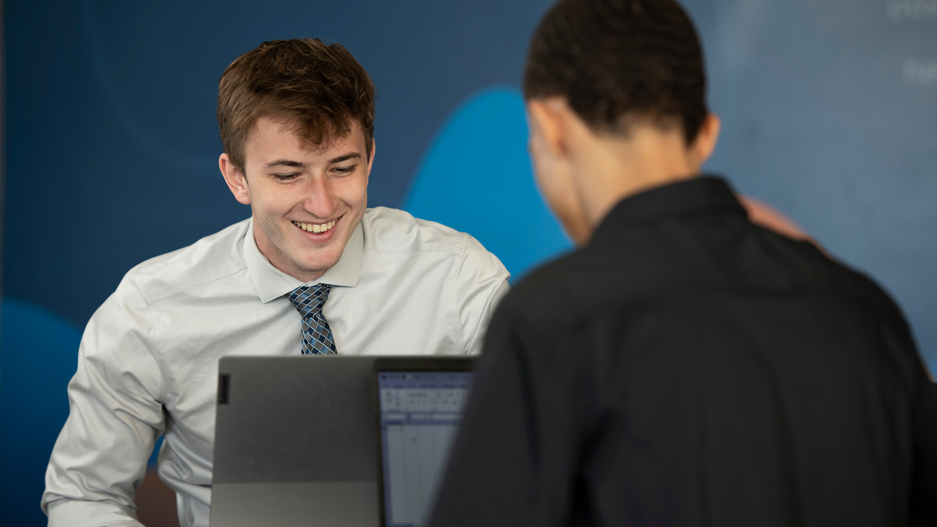 Two Drake Business/Law 3+3 students in dress shirts collaborate on a project while using laptops