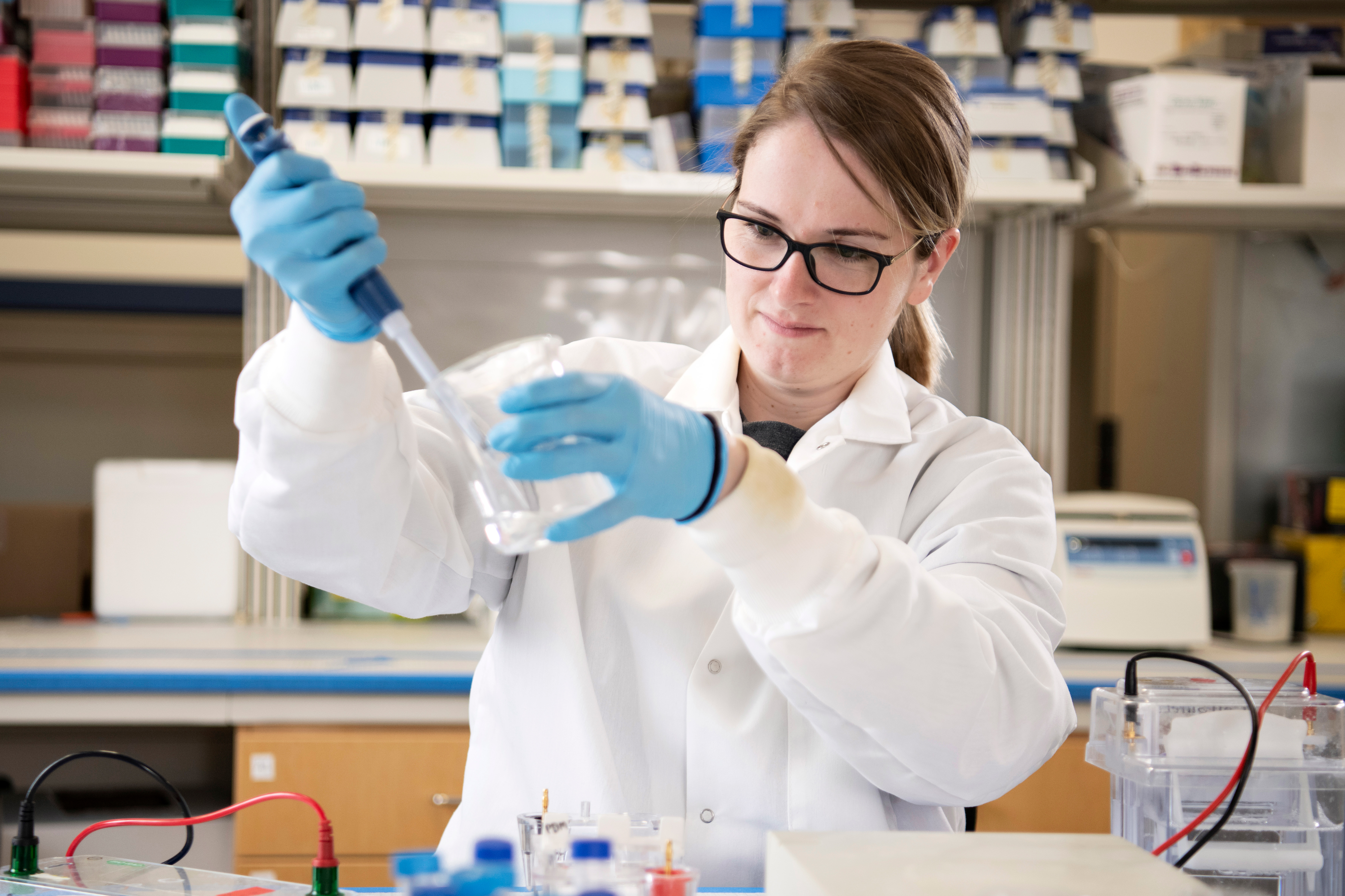 In a campus lab, a Drake Chemistry student uses a syringe to draw liquid from a beaker they're holding