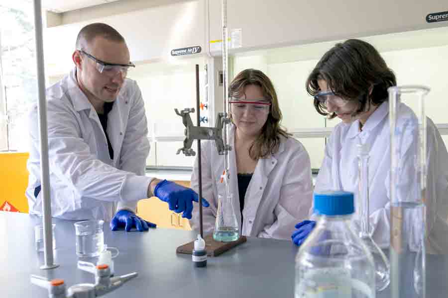 A faculty member instructs two Drake Chemistry majors in fluid measuring principles in a campus research lab