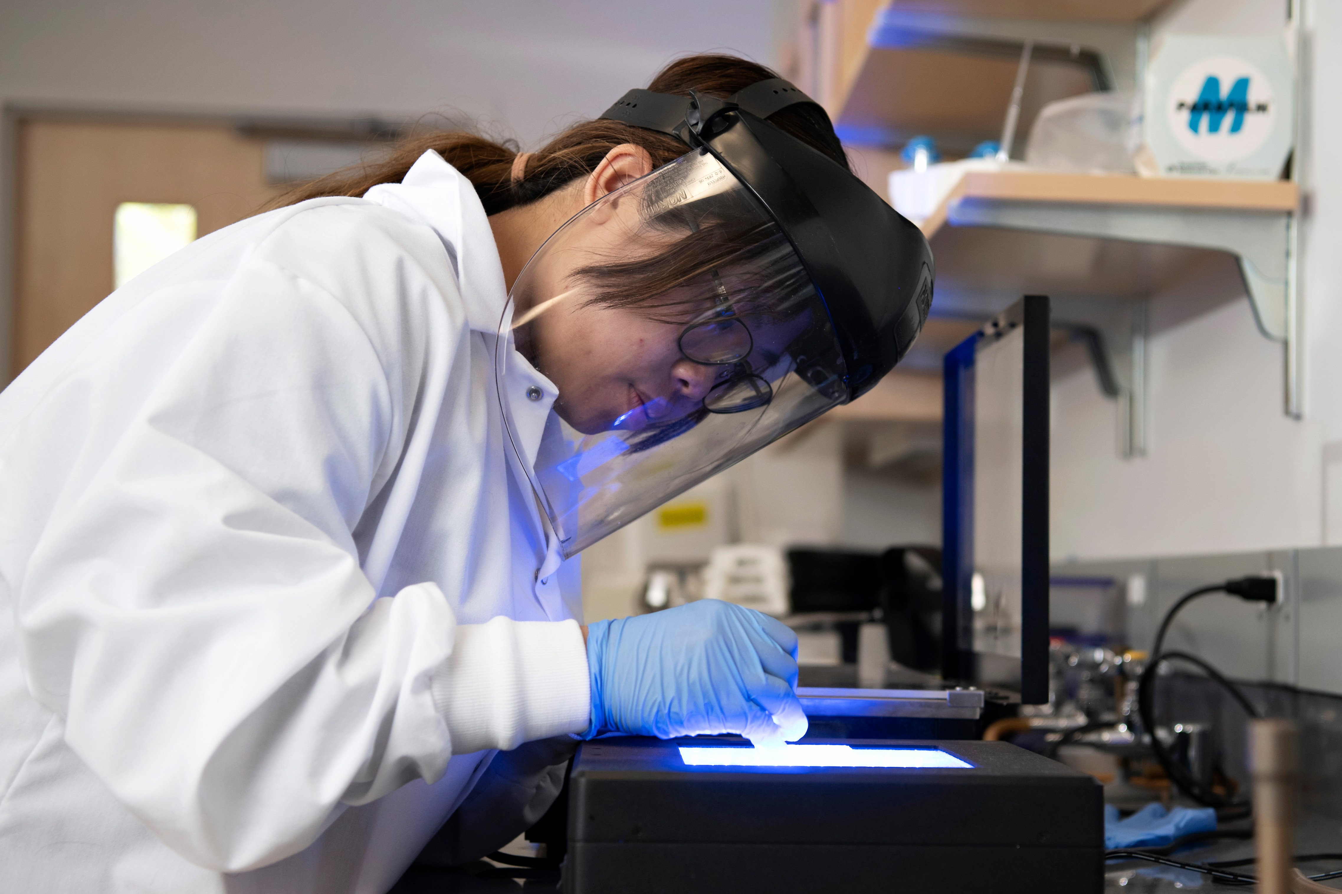 For a research project, a Drake Chemistry student wears a face shield and gloves to examine samples in a light box