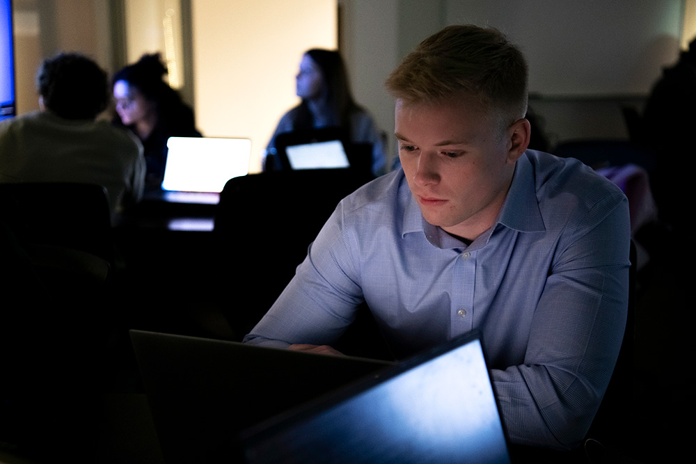 Drake Computer Science majors review coursework over well-lit laptops in a dark campus computer lab
