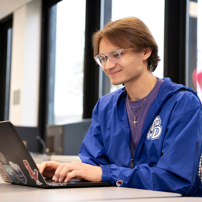A Drake Creative Writing major smiles while typing an assignment on their laptop