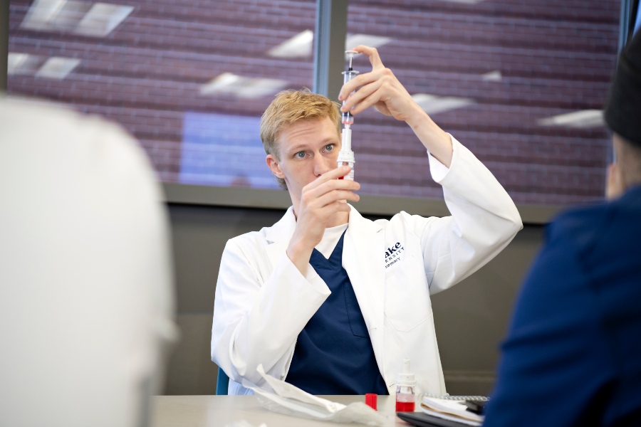 A Drake PharmD student in a lab coat practices drawing diabetes medication from a vial in a classroom