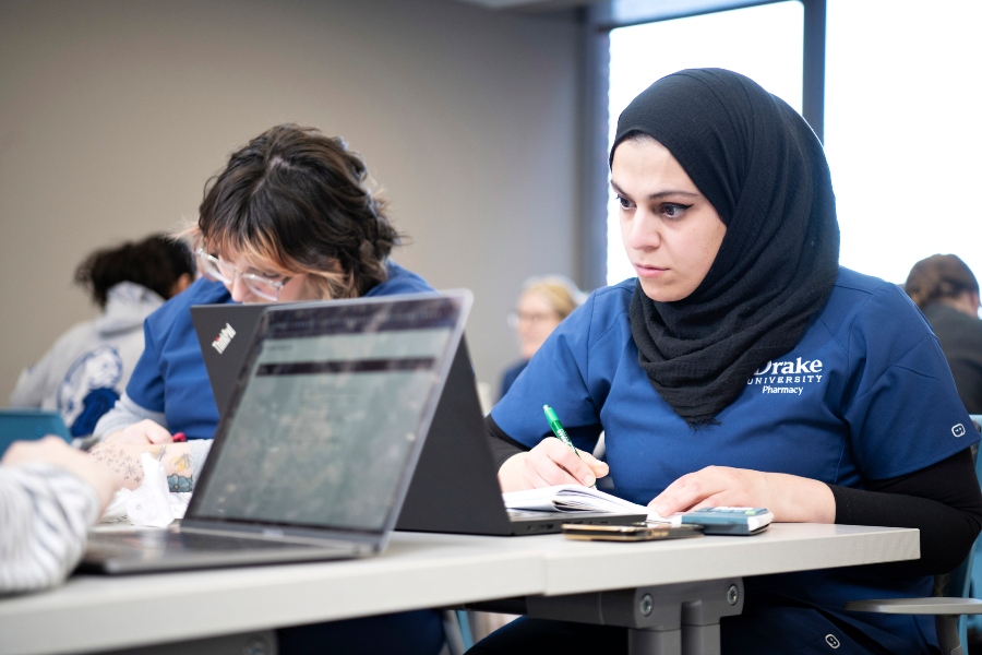 Sitting behind desks, Drake Diabetes Concentration students wearing school scrubs review course information presented on a tablet