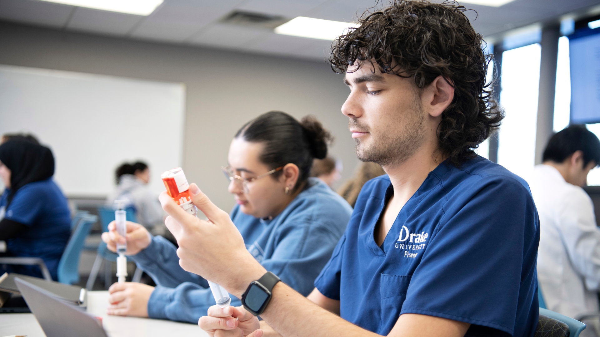 Sitting behind a lab table, Drake students pursuing the Diabetes Concentration practice drawing medication from a vial