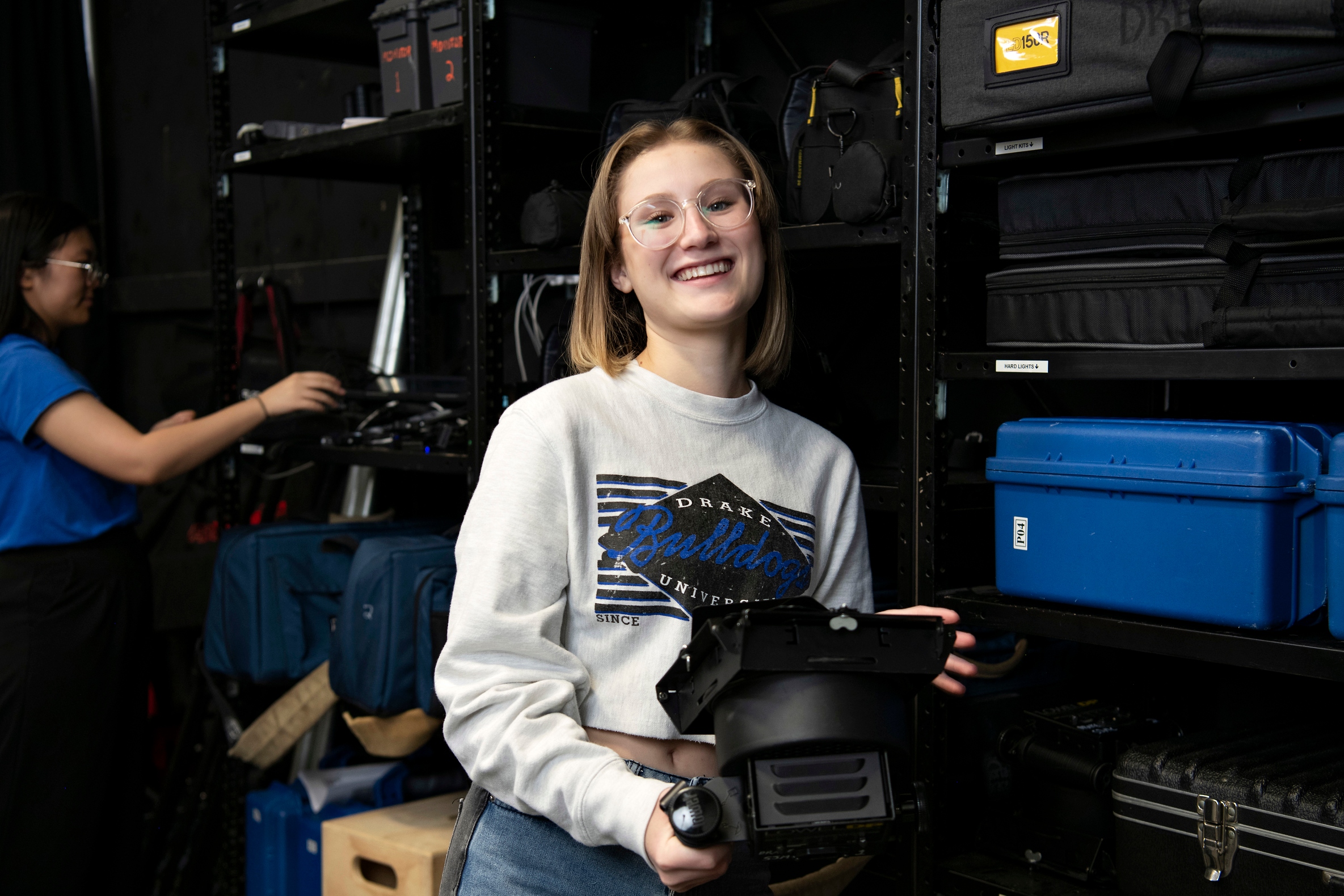 A Drake University Digital Media Production major smiles as they adjust a light during a campus production