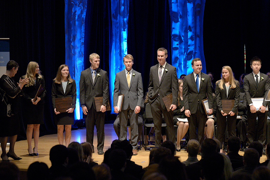 A group of Economics majors stand on stage, in suits, with their award certificates at their sides
