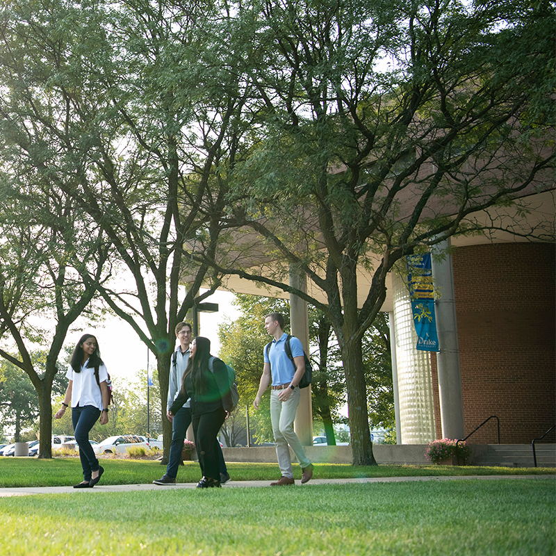 A group of Drake Economics majors wander outdoors along a path past a few trees