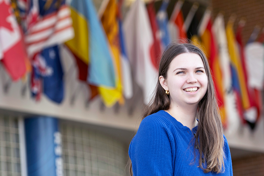 A Drake Economics major smiles while standing outdoors in front of a series of international flags