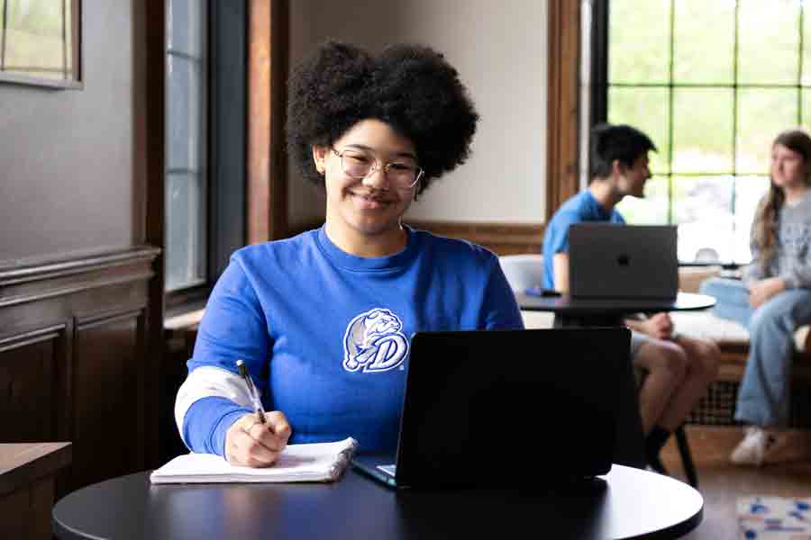 A Drake English major completes a paper, with their notebook and laptop, in a campus common area
