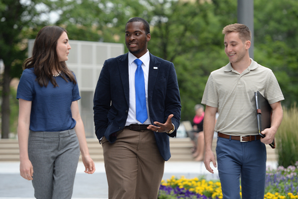 Three Entrepreneurship minors, one in a suit and tie and the other two in business casual dress, converse as they walk through Drake University's campus