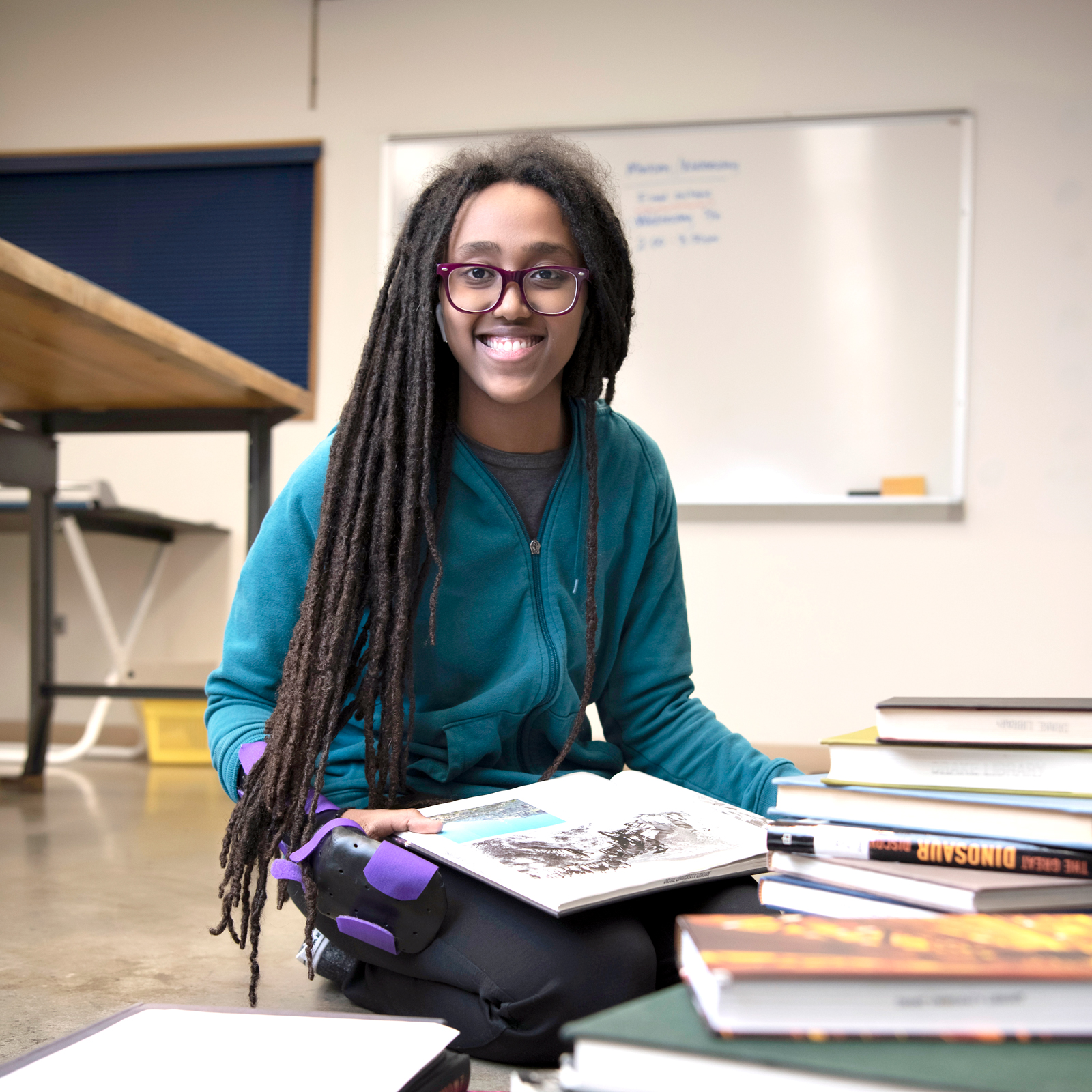Sitting cross legged in a classroom, a Drake Graphic Design student reviews art books for inspiration