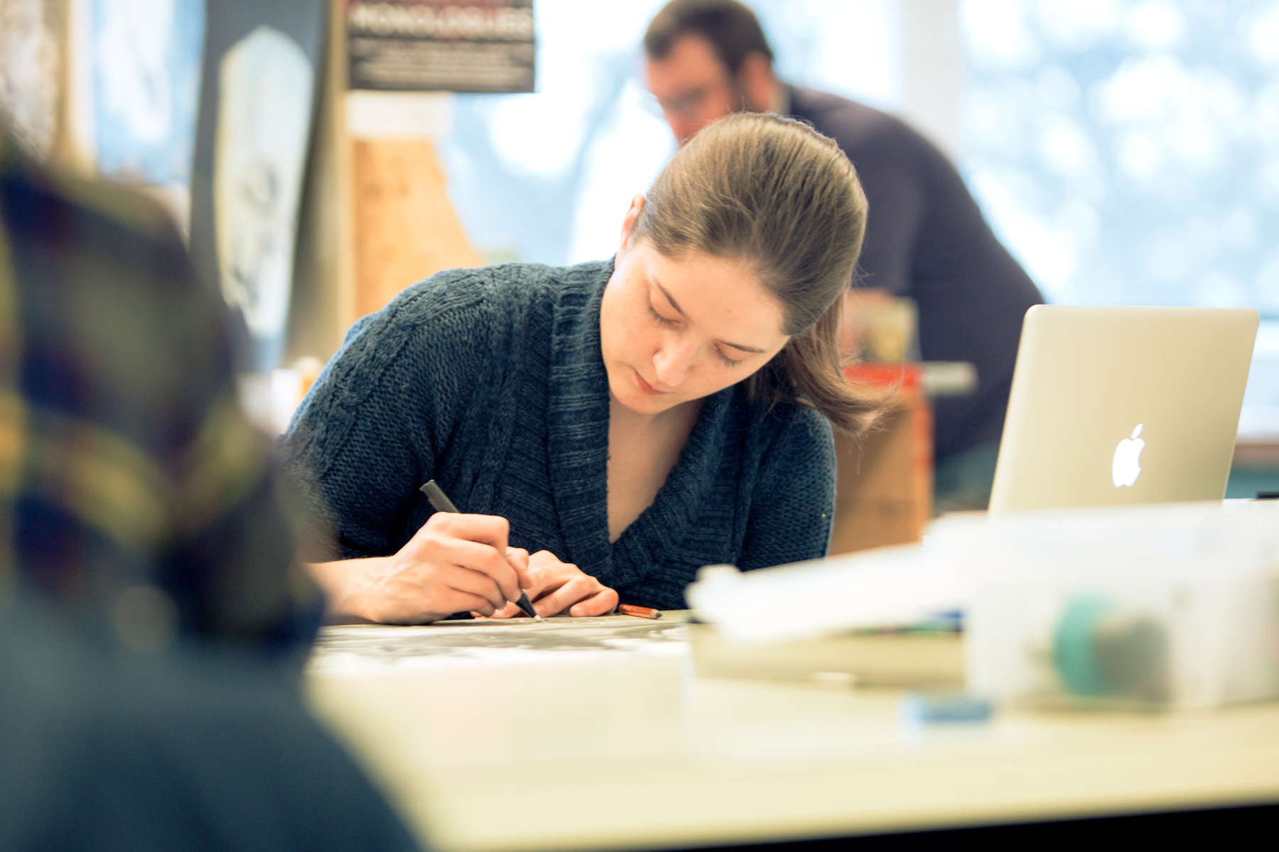 A Drake Graphic Design student hashes out in idea in their notebook while sitting in front of a laptop