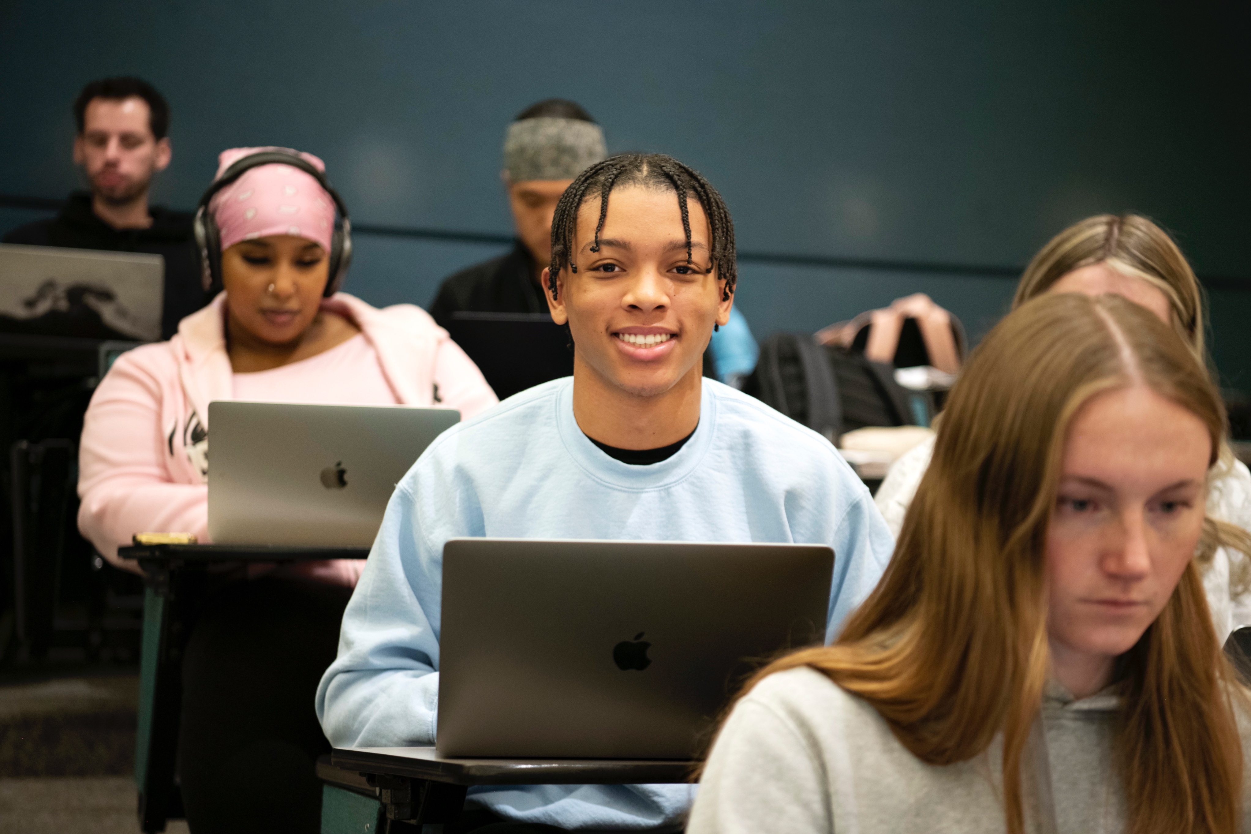 Drake Health Sciences majors sitting in rows of classroom desks smile while using their laptops
