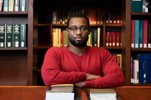 A Drake history student folds their arms while sitting behind the table in a library