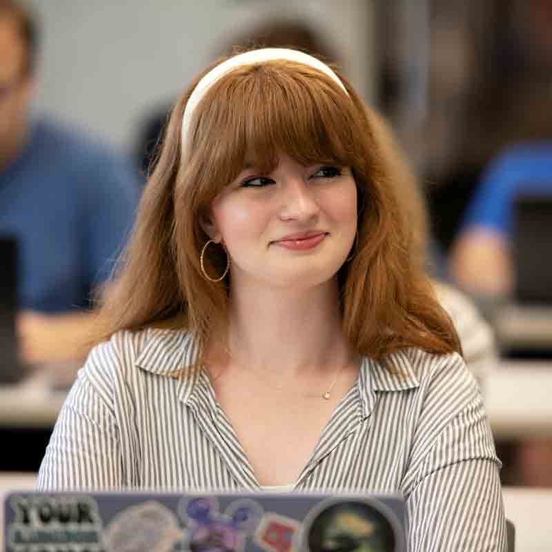 A Drake history student using a laptop with stickers looks sideways in class
