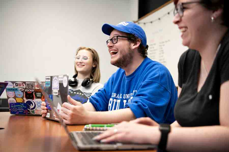 Drake History students gathering around a table with their laptops brightly smile as they discuss a service learning project