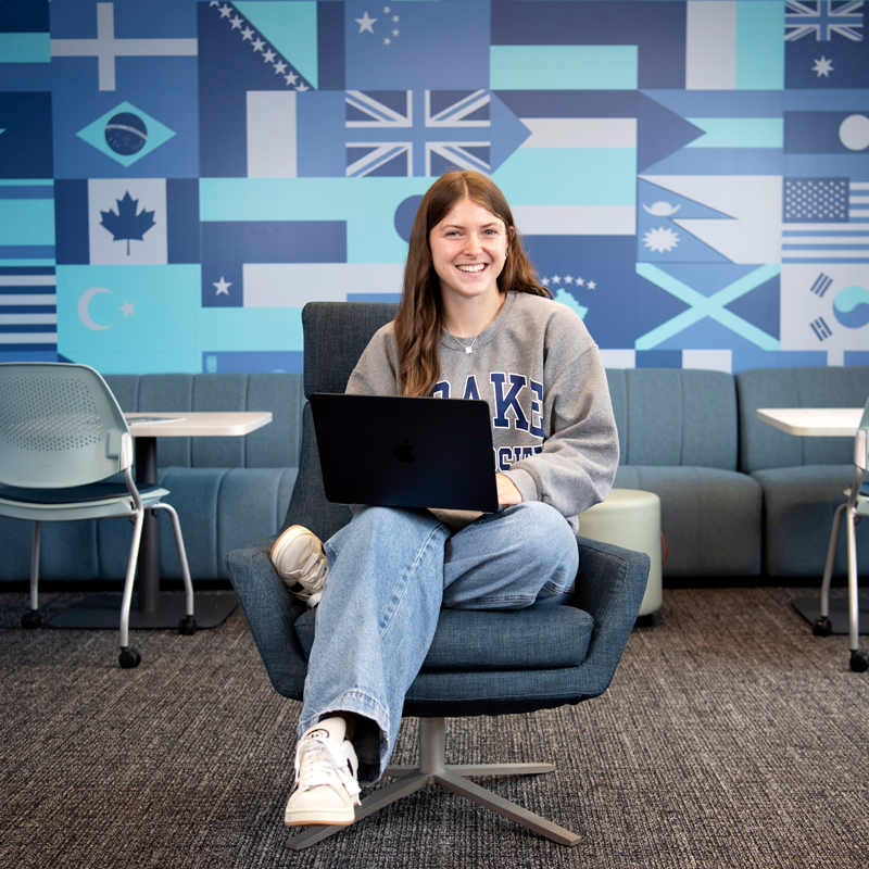 A student from Drake's Human Rights Studies Minor works on a laptop in a room with blue-tinted international flags