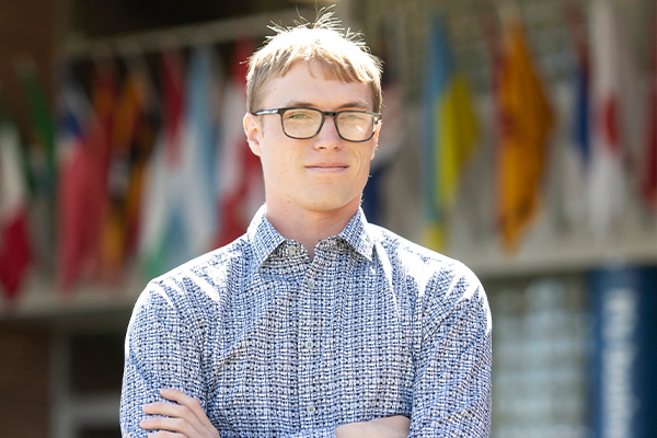 A Drake Information Systems major in glasses crosses their arms while standing outdoors on a sunny day