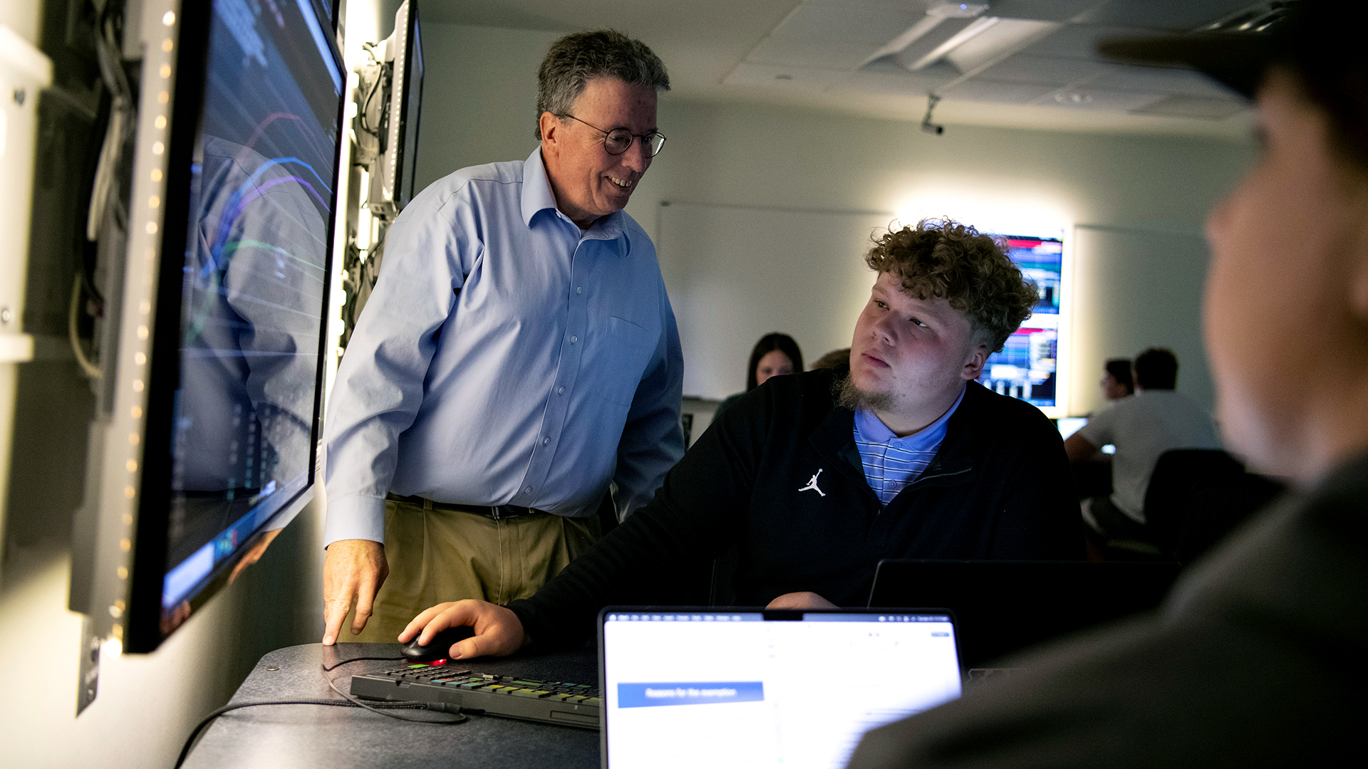 A professor helps two Drake Information Systems majors examine data displayed on a large monitor in a computer lab