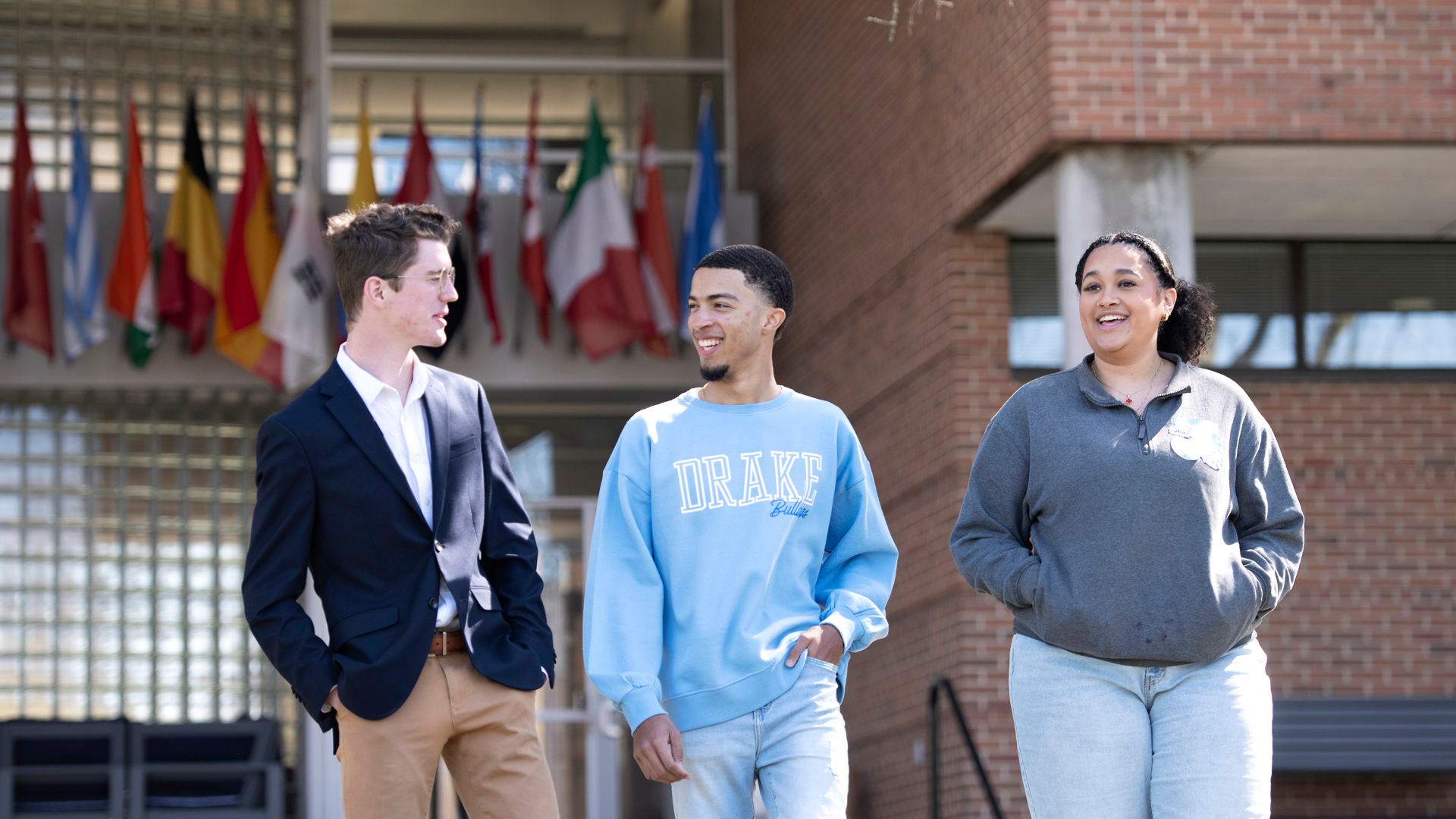 Three Drake International Relations students have a discussion outside a brick building with flags