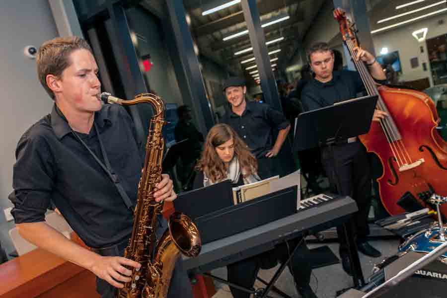 A jazz combo consisting of a saxophone, upright bass, and keyboard rehearses in a campus performance space