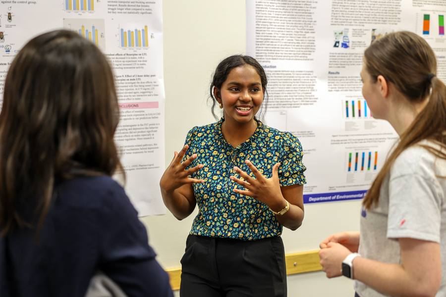 A Drake student explains their Kinesiology research project, talking in front of their poster, to a group of students