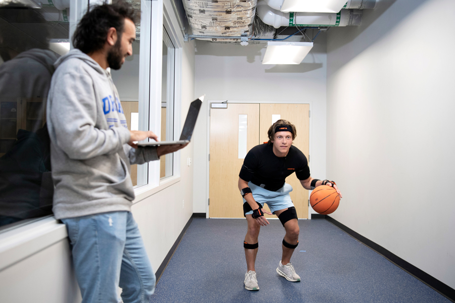 For a research project, one Kinesiology major bounces a ball down a hallway in a Drake laboratory, while another student takes notes on their laptop