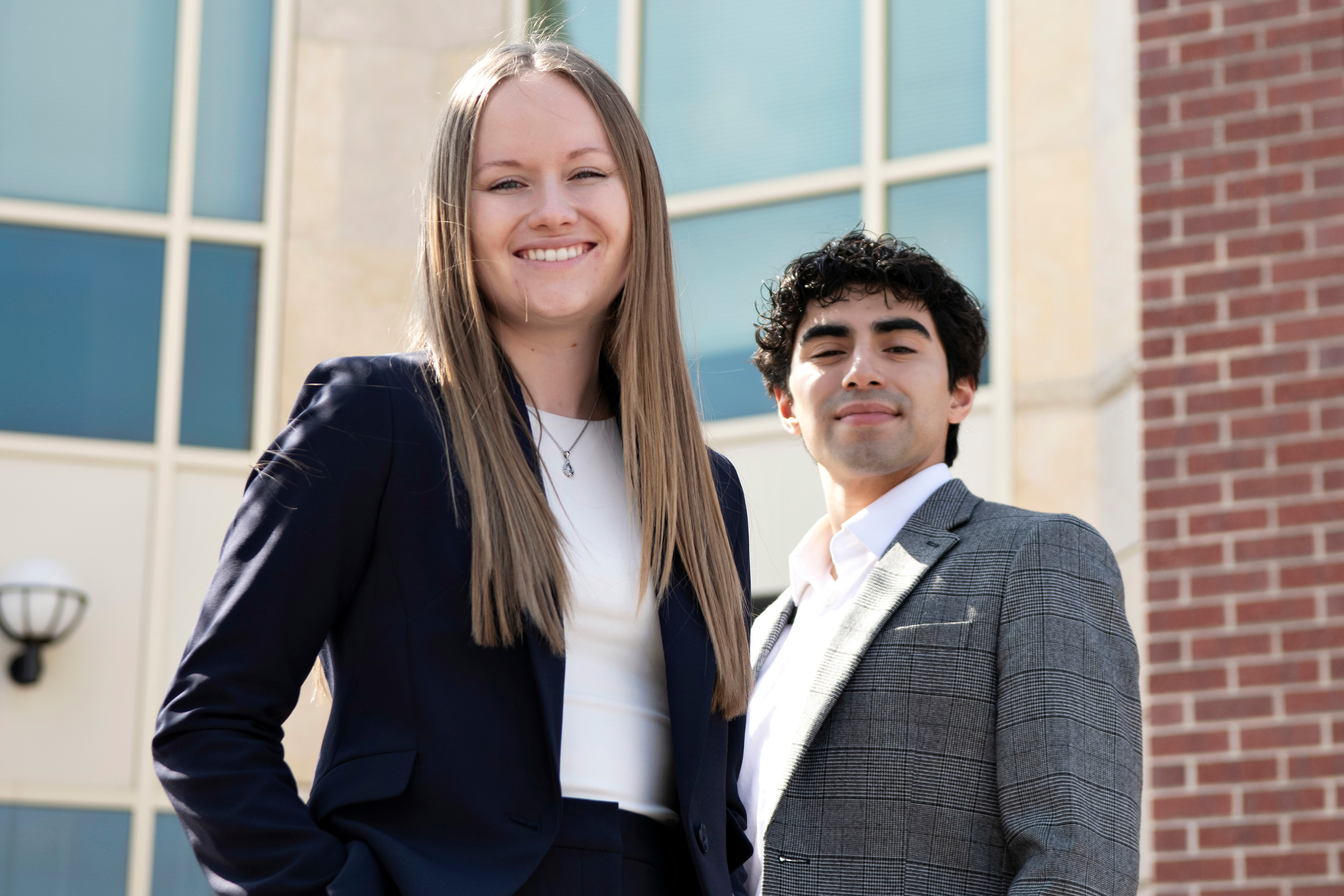 Two Drake Law, Politics, and Society students in blazers smile as they stand in front of a windowed building
