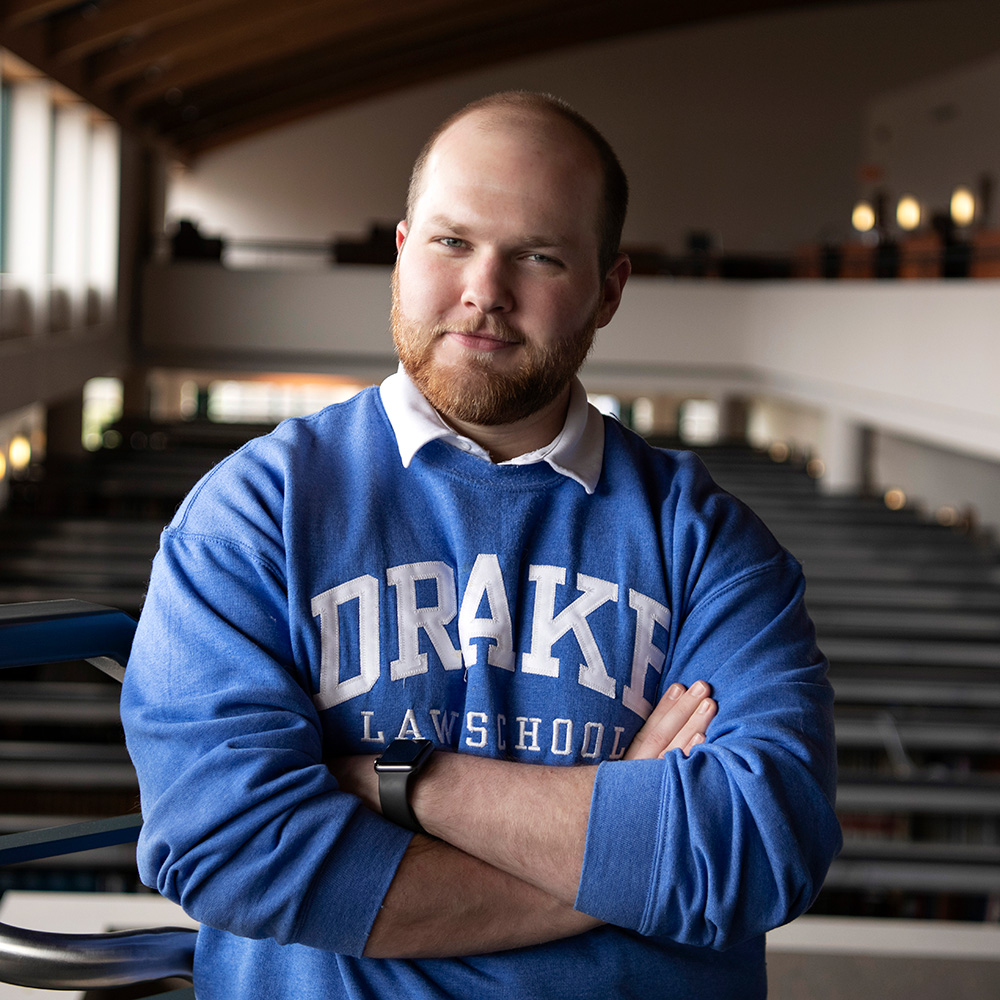 A student wearing a Drake sweatshirt crosses their arms while standing in an auditorium balcony