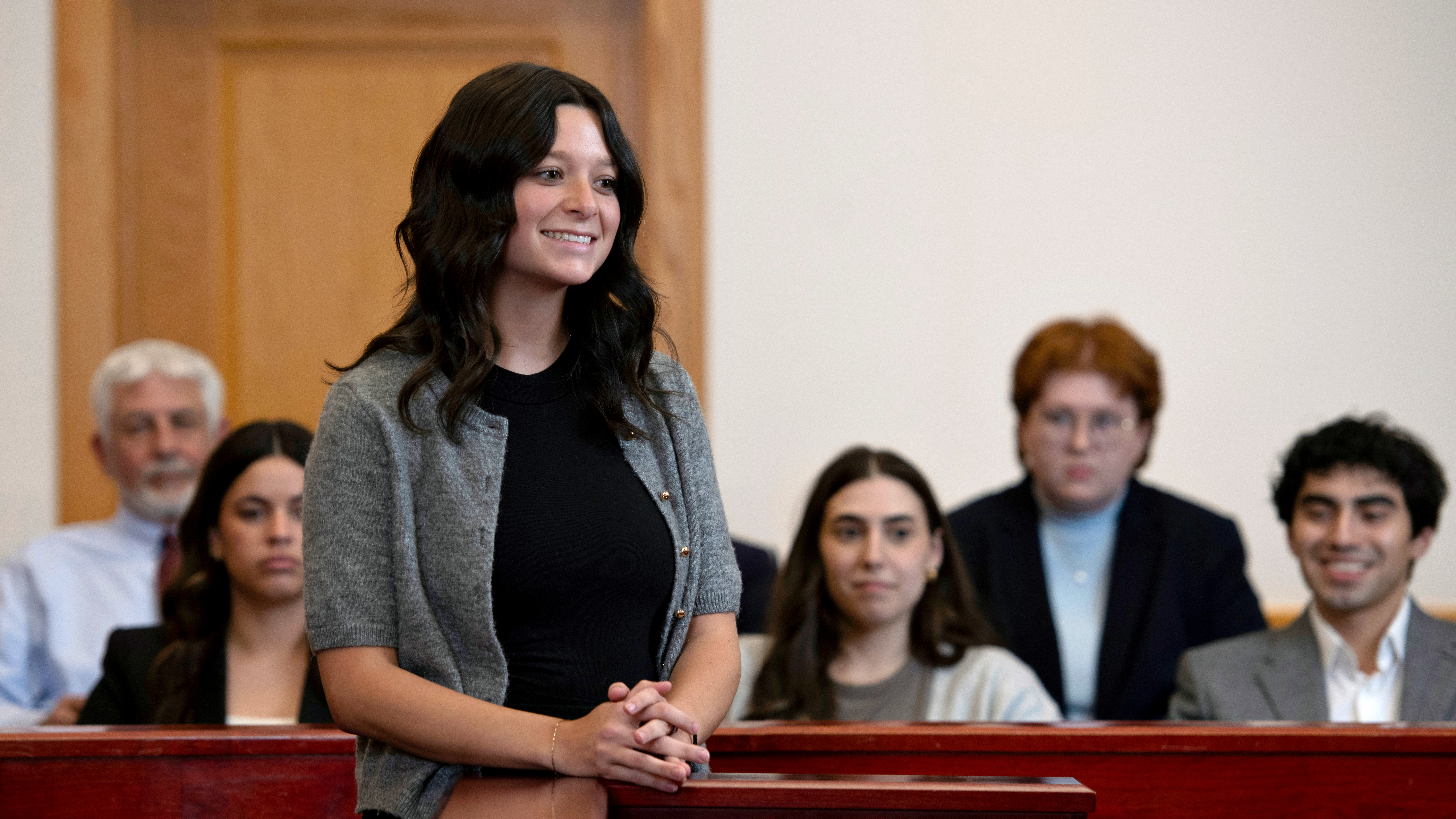 A student from Drake's Law, Politics, and Society program smiles while standing in front of a mock courtroom jury