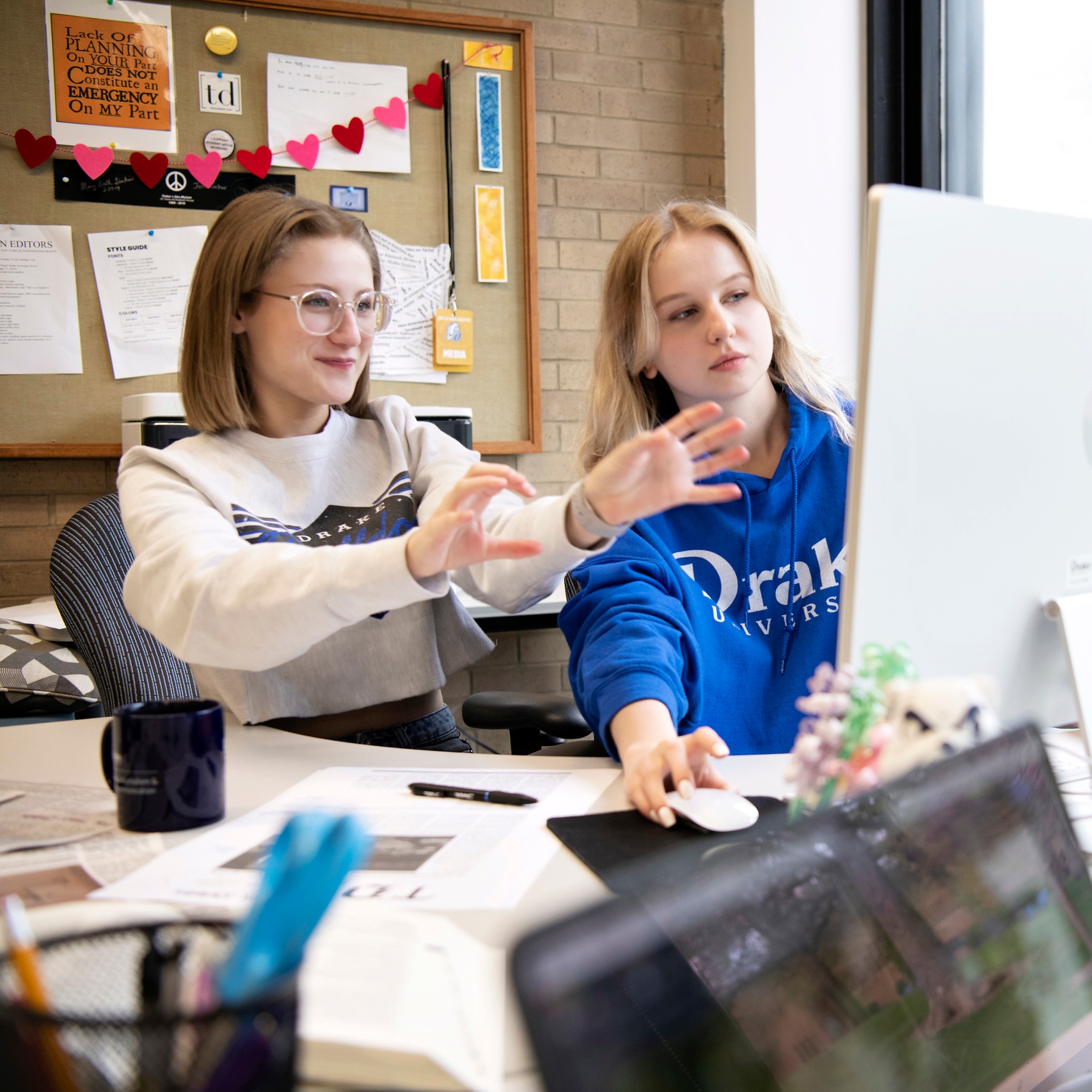 Two Drake Magazine and Brand Media Majors collaborate on a project in front of a computer monitor