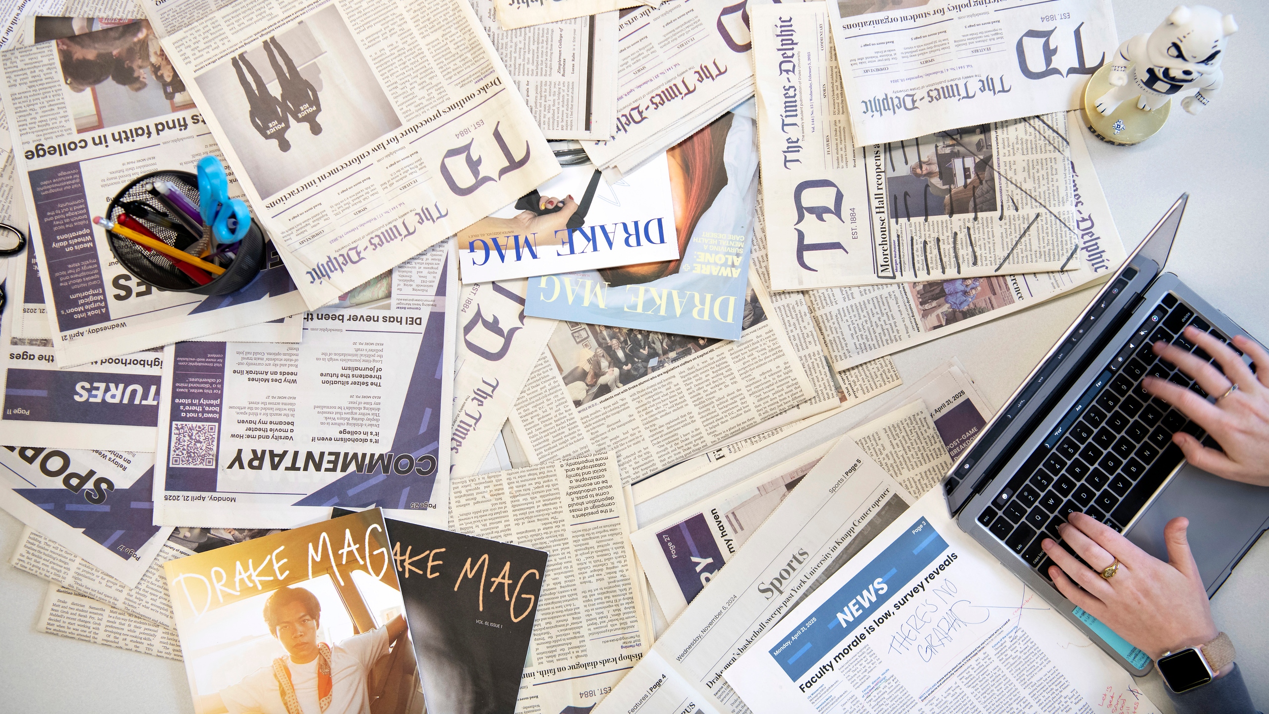 A student from Drake's Magazine and Brand Media program works on a laptop near a group of student publications