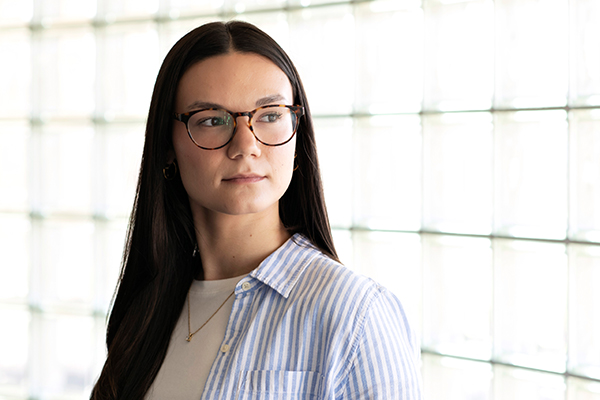A Drake Management and Organizational Leadership student in glasses and a striped shirt looks to the right in a well-lit room