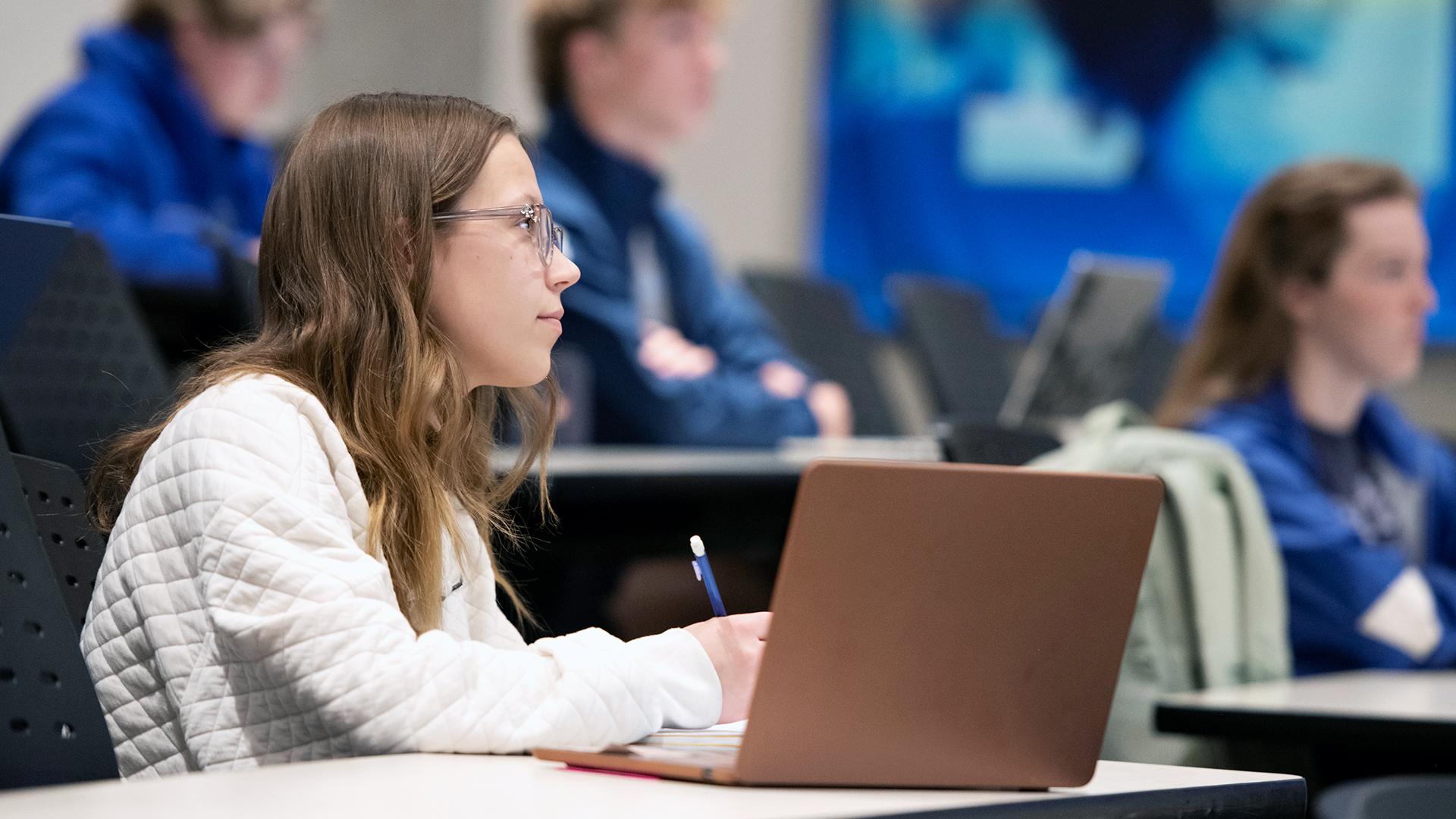 In class, a Drake Management and Organizational Leadership Major writes notes on a notepad while their laptop sits nearby