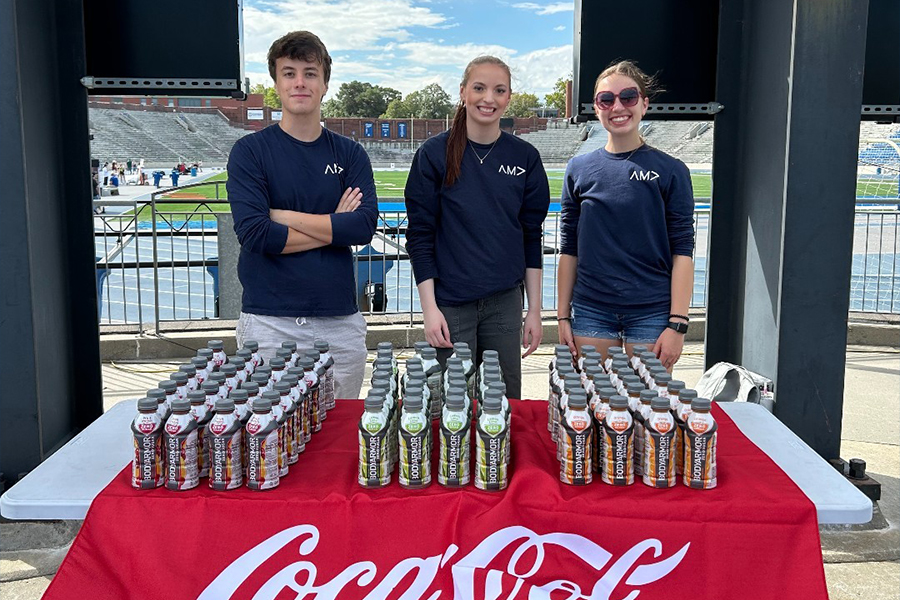 Drake Marketing majors stand by a table with a Coca-Cola tablecloth and Bodyarmor bottles as part of the AMA Integrated Marketing Communications Strategy program