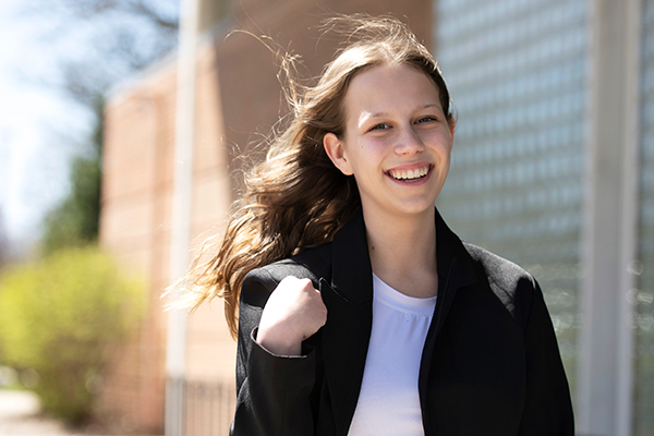 A Drake Marketing major in a black blazer pulls their hand close while their hair blows in the wind outdoors