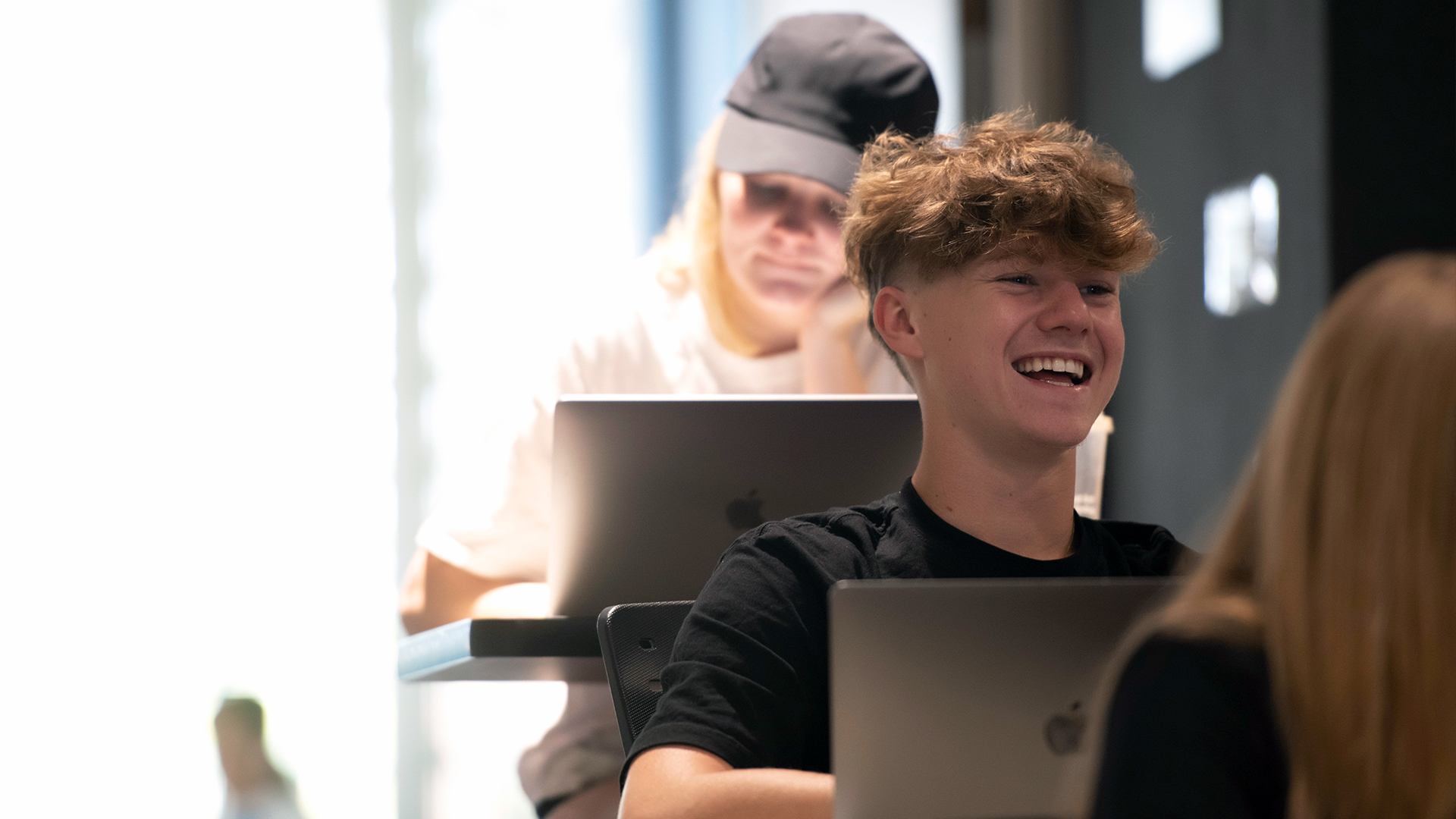 A Drake Marketing major leans back to smile and laugh while using their laptop in class