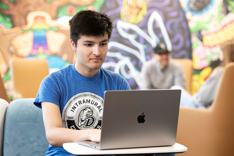 In a colorful common area, a Drake Mathematics Student analyzes research data on their laptop