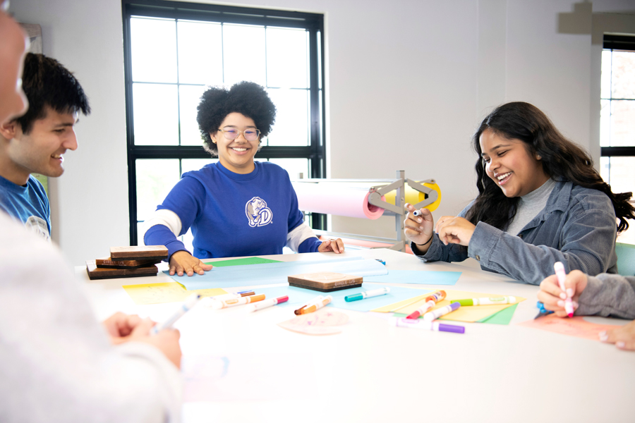 Sitting around a table, Drake Mathematics students put together club fliers with markers and paper