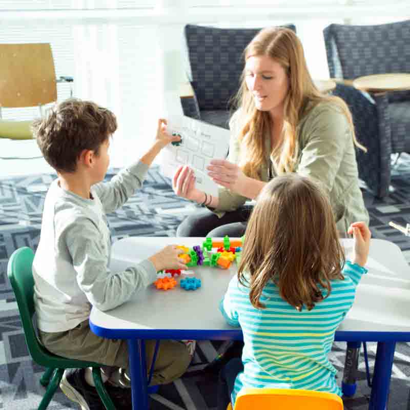 A student in Drake's Mathematics for Secondary Education program helps two elementary-grade students understand a mathematics concept in a colorful classroom