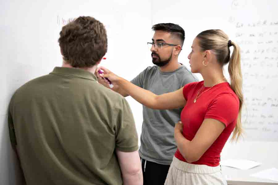 Standing in front of a whiteboard, three students enrolled in Drake's Mathematics for Secondary Education program discuss the results of an equation
