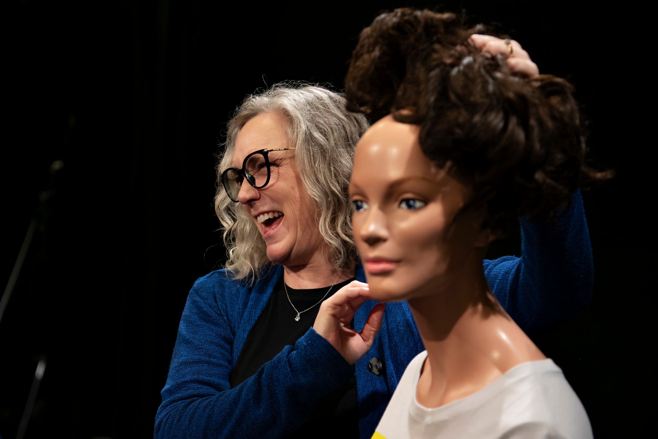 A professor for Drake's Multimedia Journalism Major removes a wig from a mannequin in a campus production setting