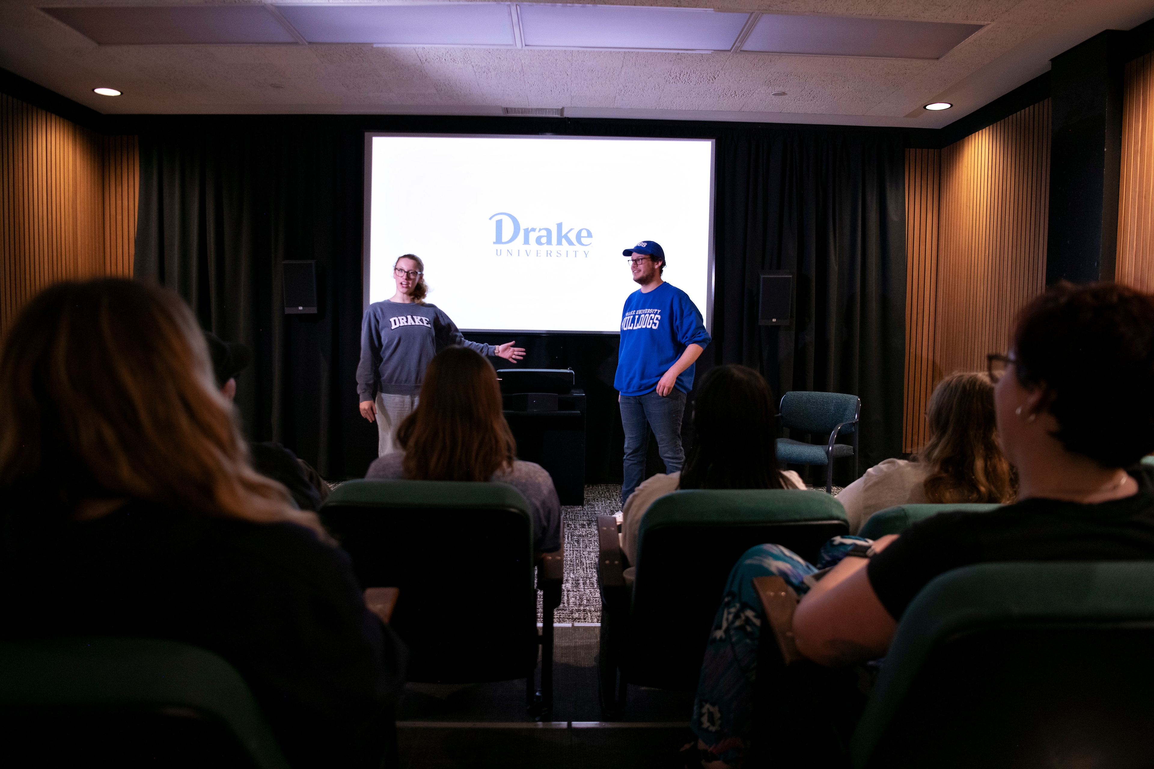 Two Drake Multimedia Journalism Majors stand in front of a screen to present their short film during the DBS 48-Hour Film Festival