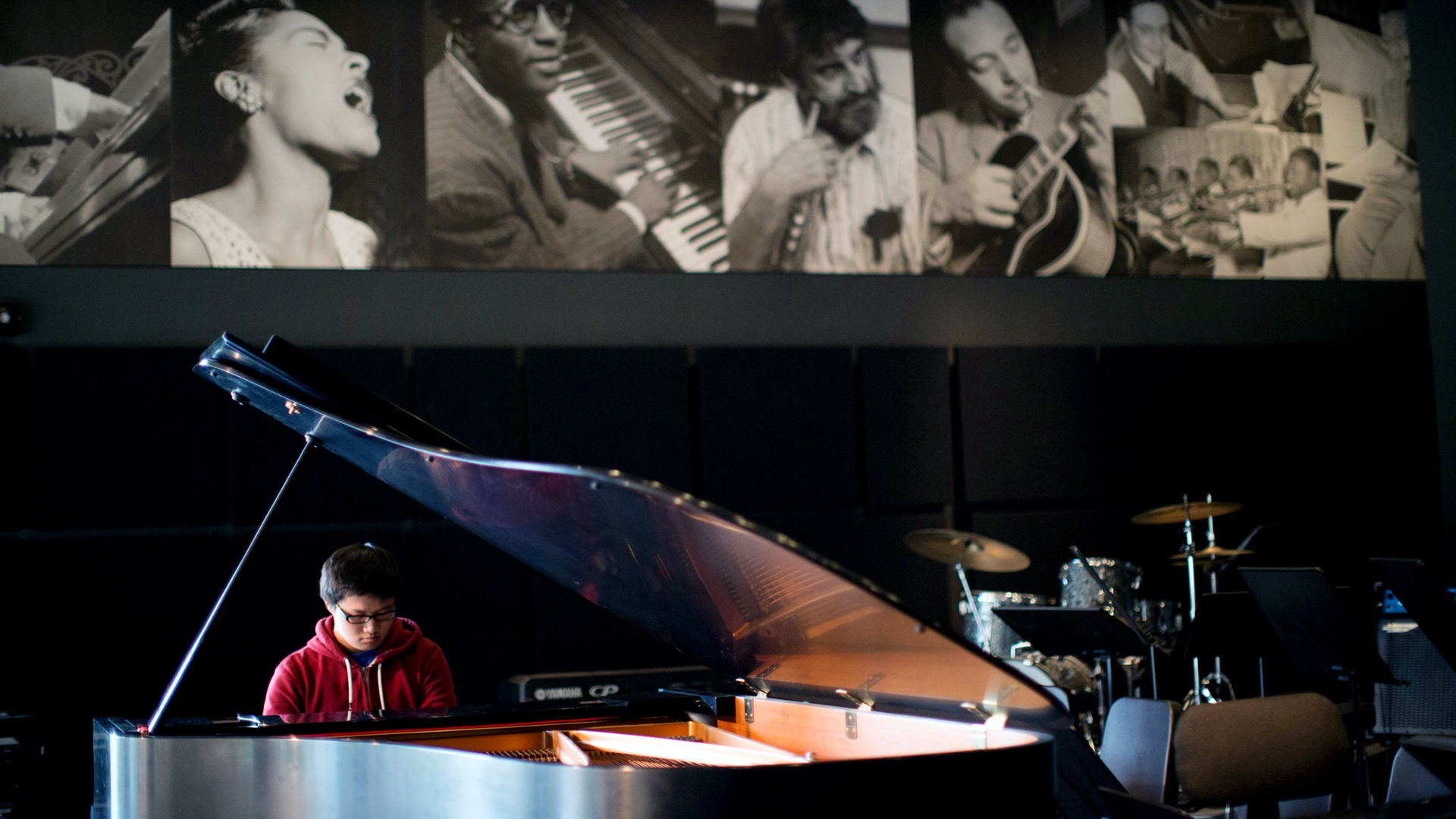A Drake Music Business student performs a recital on a grand piano situated in a hall with photographs of other musicians