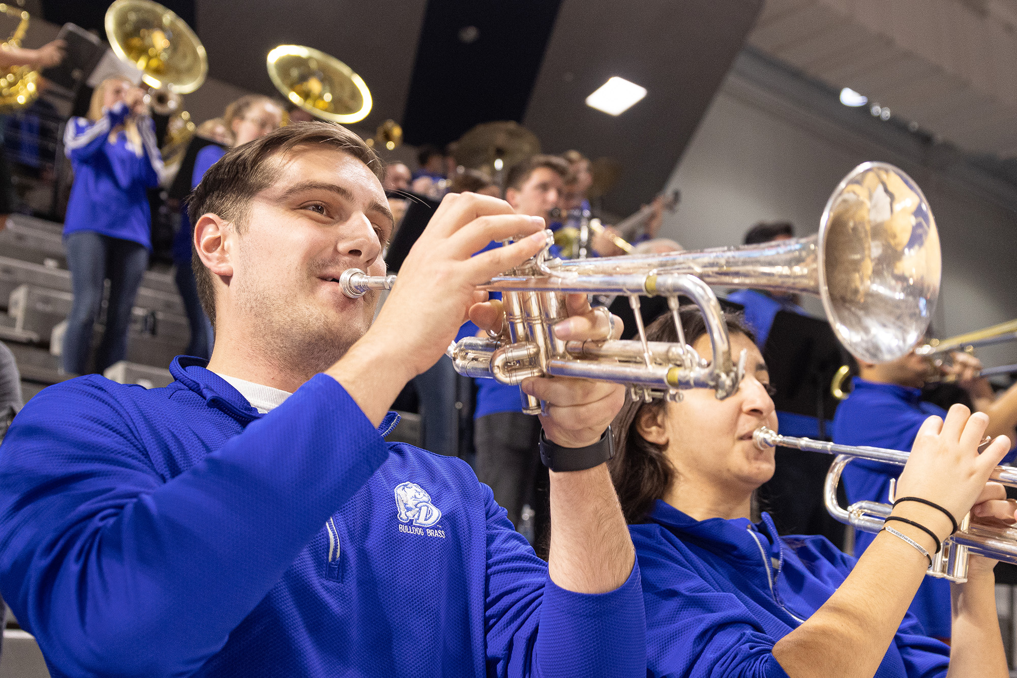 Drake Music Education majors in blue sweatshirts play trumpets in the school's marching band during a basketball game