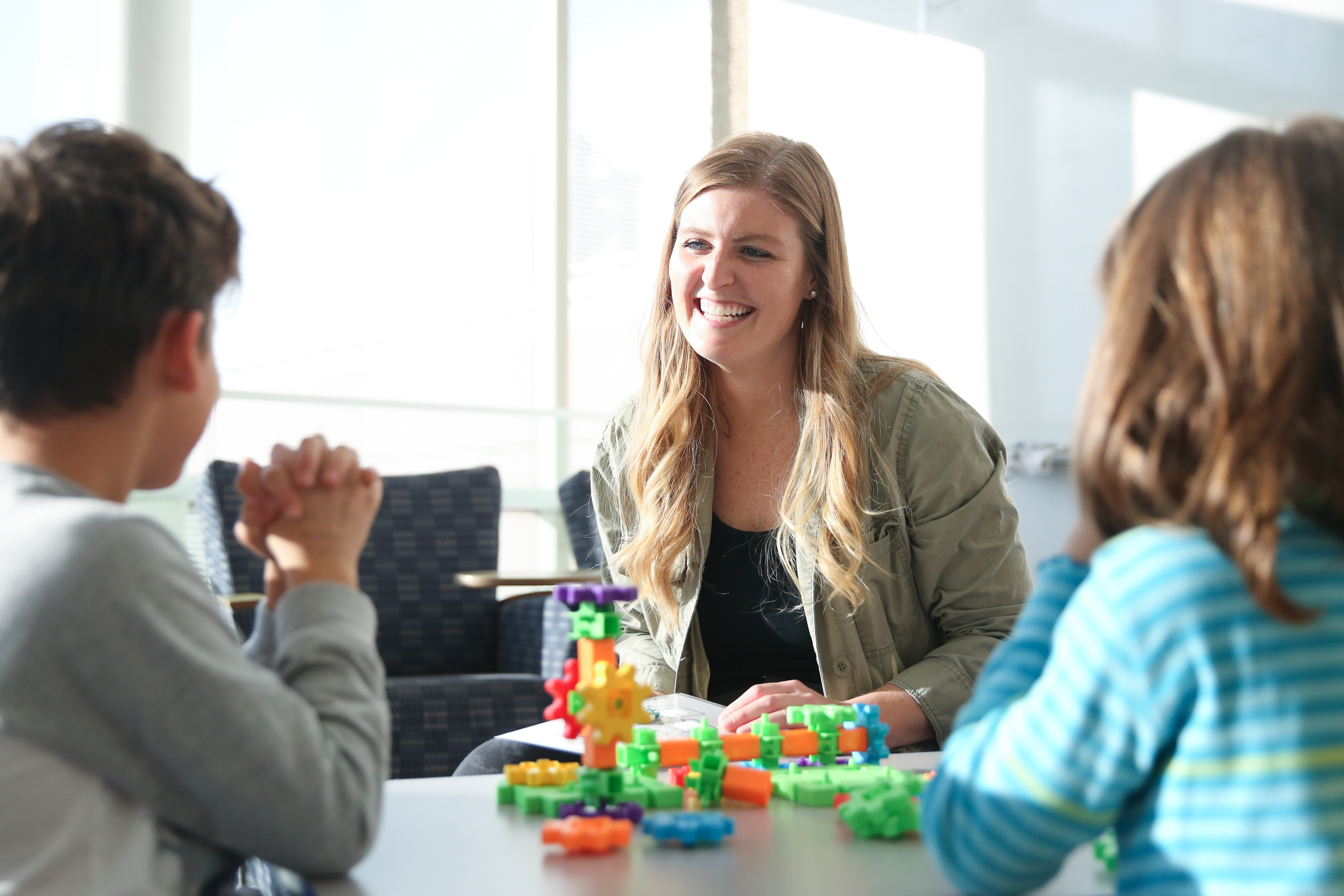 A student from Drake's Music Education program smiles at students sitting on the other side of a child-size table covered in toys