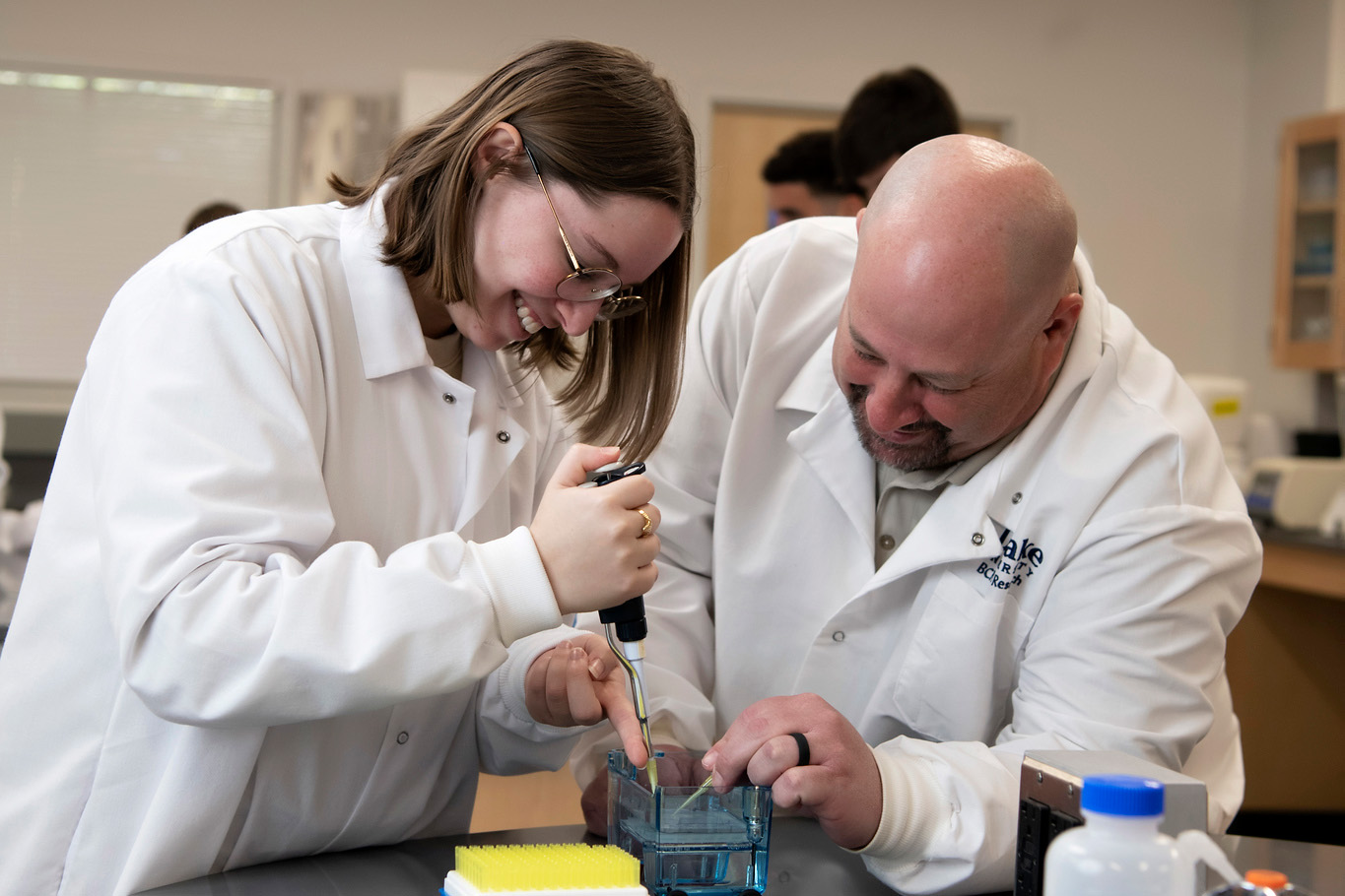 A professor guides a Neuroscience student at Drake learning to draw fluid from a container with a syringe